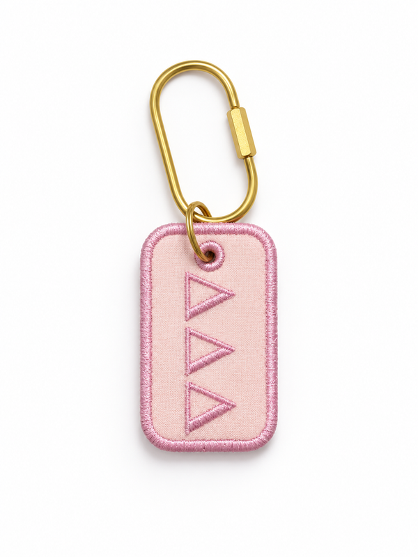 A pink rectangular embroidered tag with a gold carabiner attached, featuring three stitched triangles down the center, shown on a plain white background.