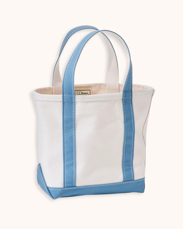 A white canvas tote bag with light blue trim and handles, featuring a small brass brand plaque on the front.