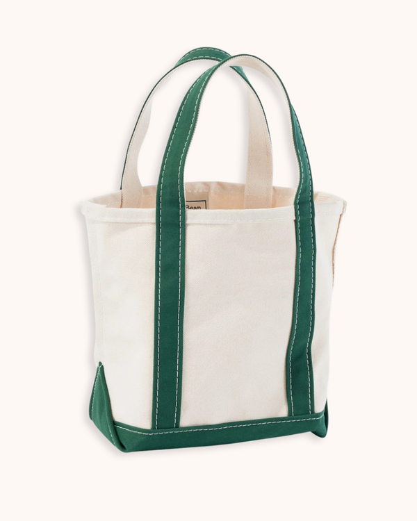 An off-white canvas tote bag with dark green handles, trim, and bottom corner accents, shown against a solid off-white background.