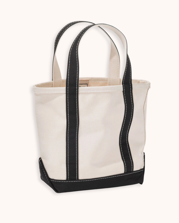 An off-white canvas tote bag with black trim and dual shoulder straps, shown against a solid off-white background.
