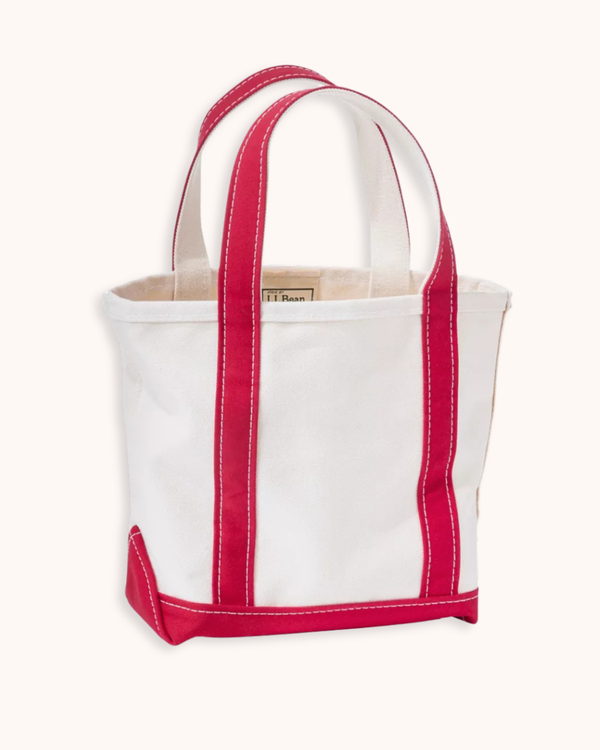 A white canvas tote bag with vibrant pink-red contrast stitching and trim, featuring two top handles and a small metal brand plaque on the front.