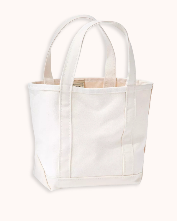 A white canvas tote bag with dual shoulder straps, shown against a solid off-white background.