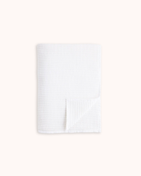 A folded white waffle-weave fabric item, likely a baby blanket or towel, shown on a solid off-white background.