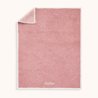 A personalized dusty pink woven blanket with a white border and the name 'Sophia' embroidered in white at the bottom, shown on a light cream background.