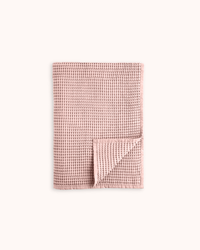 A folded dusty pink waffle-weave towel with a textured grid pattern, shown on a clean off-white background.