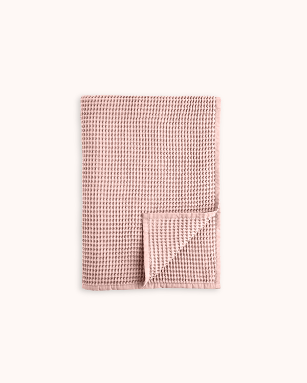 A folded dusty pink waffle-weave towel with a textured grid pattern, shown on a clean off-white background.