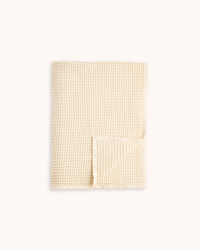 A folded cream-colored waffle-weave fabric item, likely a towel or blanket, shown on a plain off-white background.