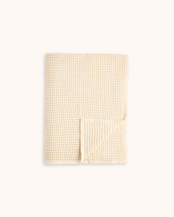 A folded cream-colored waffle-weave fabric item, likely a towel or blanket, shown on a plain off-white background.